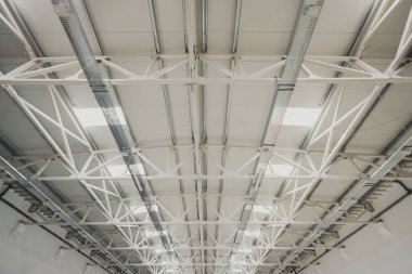 Büyük bir sanayi binasını destekleyen beyaz boyanmış metal çatı iskeleti.