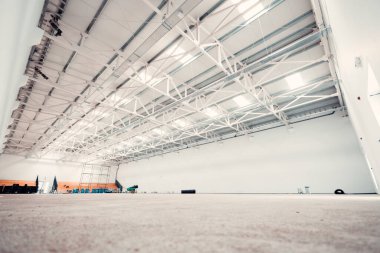 Metal çatı yapısı ve beton zemini olan içi boş bir deponun geniş bir manzarası var.