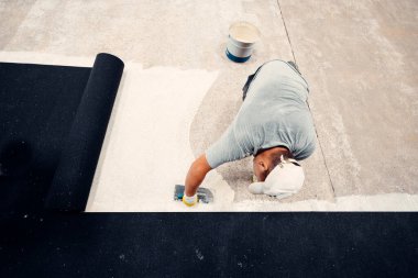 İnşaat işçisi beton zemine su yalıtımı malzemesi serpiyor.