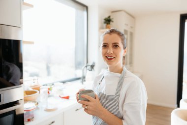 Kadın ara veriyor ve modern mutfağında sıcak bir içeceğin tadını çıkarıyor.