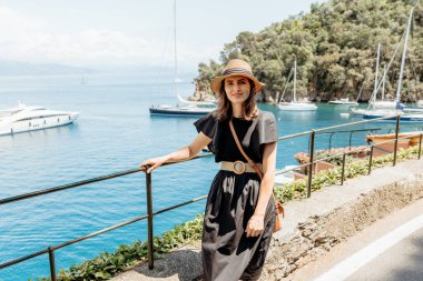 Turist, Portofino, İtalya 'nın pitoresk limanı boyunca sakin bir yürüyüş yapıyor. Lüks yatların ve büyüleyici kasabanın manzarasının tadını çıkarıyor.