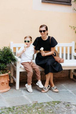 Anne ve oğlu Portofino, İtalya 'da güneşli bir günde bankta oturmuş dondurma yiyorlar.