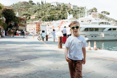Genç çocuk Portofino, İtalya 'da güneşli bir günün tadını çıkarıyor. Arka planda lüks yatlar var.