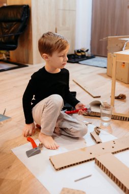 Genç bir çocuk yerde karton bir oyuncak evi kurmaya odaklanmış.