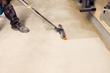 İnşaat işçisi, beton zemindeki tozları epoksi kaplama için temizliyor.