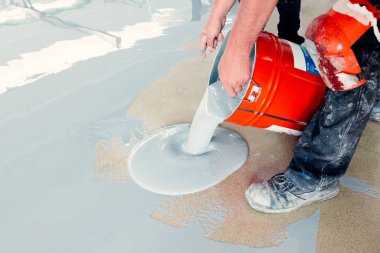 İnşaat işçisi, parlak yeni bir yer yaratmak için kovadan epoksi reçinesi döküyor.