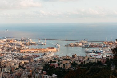 Genova, İtalya limanının havadan görünüşü, yolcu gemileri, feribotlar ve güneşli bir gökyüzünün altındaki şehir manzarası.