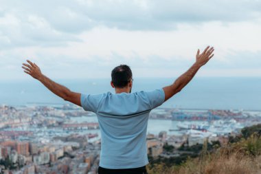 Kollarını açan ve Genova şehir manzarası ve limanı manzarasının keyfini çıkaran bir adam.