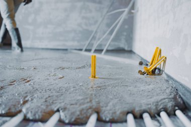 İnşaatçı zeminin altındaki ısıtma sisteminin üzerine beton döşeme döşeyerek kendi seviyesini yükselten bir bileşik ve sarı işaretleyiciler kullanıyor.