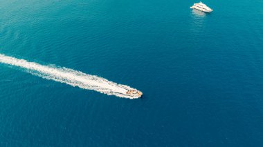 Açık mavi denizde beyaz bir iz bırakan bir teknenin havadan görüntüsü. Uzakta başka bir tekne var.