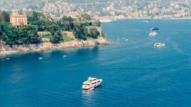 Beyaz yat, güzel bir sahil şeridi ve yemyeşil bitki örtüsüyle Camogli, Liguria 'nın mavi sularında yüzüyor.