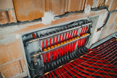 Yeraltı ısıtma sisteminin kırmızı ve siyah plastik boruları bir yerleşim yerindeki su sıcaklığını düzenleyen bir manifolda bağlıdır.