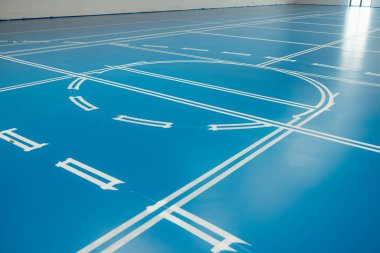 İşaretleme çizgileri yapışkan bantla bir spor salonunun yeni kaplanmış mavi epoksi zeminine uygulanıyor.