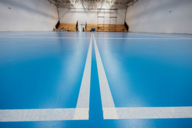 Spor salonunun yeni boyanmış mavi epoksi zemininde oyun alanını gösteren beyaz çizgiler, son zamanlardaki yenileme veya inşaat çalışmalarını gösteriyor.