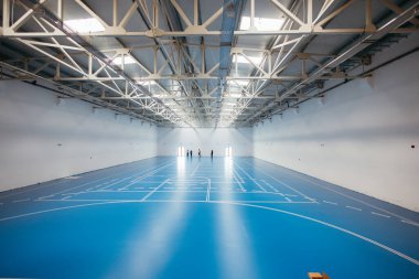 Mavi epoksi reçine zeminli boş spor salonu ve yeni uygulanan kaplamayı inceleyen işçiler.