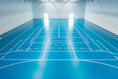 Beyaz çizgiler mavi epoksi bir zemindeki farklı spor alanlarını işaret ediyor. Boş bir spor salonunda.