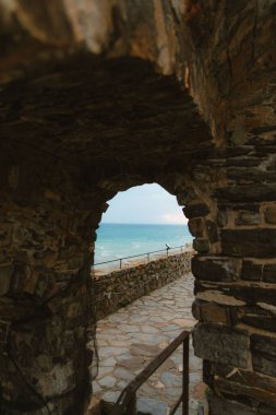 Monterosso al mare 'deki taş kemer deliğinden geçen ligurian denizinin manzarası, asfalt bir yol ve metal bir korkuluk içeriyor.