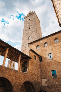 San Gimignano 'nun tarihi merkezinde ortaçağ mimarisi, bulutlu bir gökyüzünün altında Torre Grossa ve Palazzo del Popolo yer alıyor.