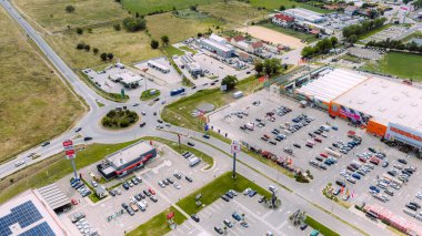 Otomobiller, park yeri ve çeşitli işletmeleri olan büyük perakende sahasının yakınındaki dolambaçlı yoldan geçiyor.