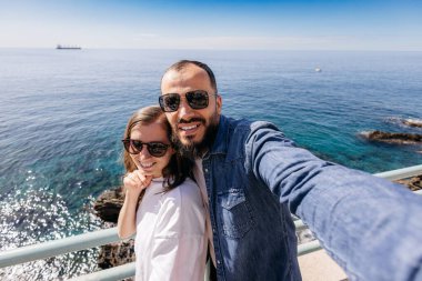 Arka planda güzel deniz manzarası olan mutlu bir çift selfie çekiyor.