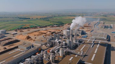 Etrafı tarımsal alanlarla çevrili kırsal bir araziyle çevrili, duman yayan bir ahşap çip enerji santralinin havadan görüntüsü.