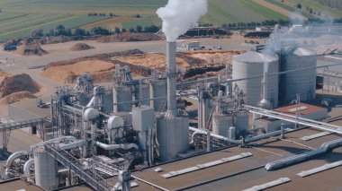 Odunları işleyen, bacalarından duman ve buhar çıkaran, endüstriyel aktiviteleri ön plana çıkaran bir kereste fabrikasının hava görüntüsü.