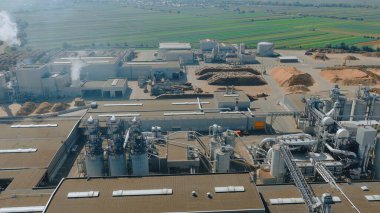 Odunları işleyen, bacalarından duman çıkaran ve kırsal alanda tarlaları olan bir kereste fabrikasının hava görüntüsü.