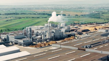 Tarımsal tarlalar ve tarım arazileriyle çevrili, duman yayan bir biyokütle enerji santralinin havadan görüntüsü.