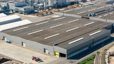 Çatı pencereleri ve yükleme rıhtımları demiryolu ve yollarla mal alan büyük bir endüstriyel deponun havadan görüntüsü.