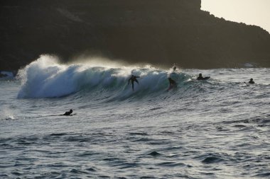 İnsanlar gün batımında okyanusta at sürüyorlar.
