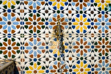 Etrafında mozaik fayanslar olan bronz su musluğu.