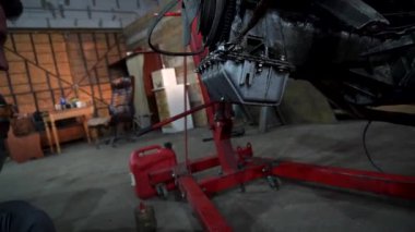 Bir tamirci tamir ve akort için kırmızı asansörde eski kirli bir araba motorunu söker.