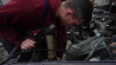 Bir tamirci tamir ve akort için kırmızı asansörde eski kirli bir araba motorunu söker.