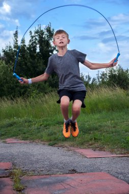 Bir çocuk mavi bir ipe atlayıp spor yapıyor.