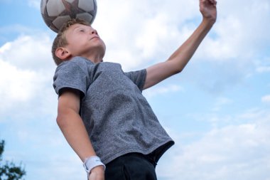 Bir çocuk futbol topuna tekme atıp kafa atmaya hazırlanıyor.