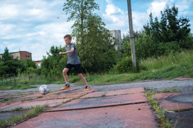 children's football, a boy of European race is studying on a green field with a ball in a blue uniform