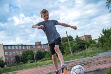 children's football, a boy of European race is studying on a green field with a ball in a blue uniform