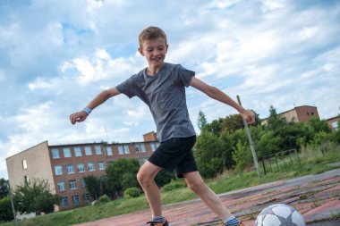 children's football, a boy of European race is studying on a green field with a ball in a blue uniform