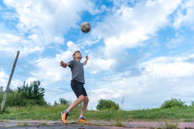 Bir çocuk futbol topuna tekme atıp kafa atmaya hazırlanıyor.