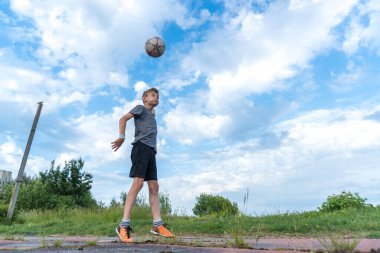 Bir çocuk futbol topuna tekme atıp kafa atmaya hazırlanıyor.