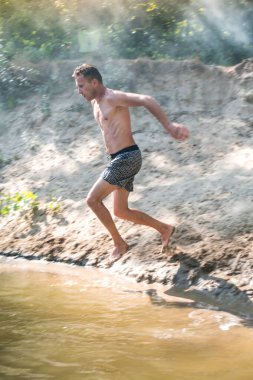 Genç bir adam daksund köpeğine sıcak bir yaz gününde nehirde yüzmeyi öğretir.