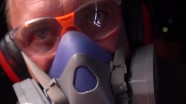 Genç adam karanlık bir odada gözleri, kulakları ve solunum organları için koruyucu ekipman kullanıyor.