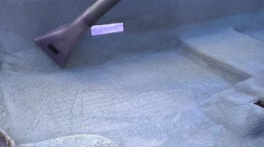 Evde elektrikli süpürgeyle çamurdan gri bir araba halısını yıkamak.