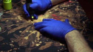 Elbiseleri akrilik boyalarla boyamak ve kumaşın üzerine mavi lastik eldivenli bir dövme makinesinin yardımıyla beyazlatıcı sürmek.