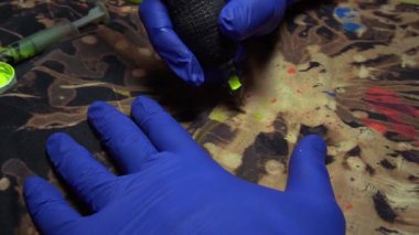 Elbiseleri akrilik boyalarla boyamak ve kumaşın üzerine mavi lastik eldivenli bir dövme makinesinin yardımıyla beyazlatıcı sürmek.