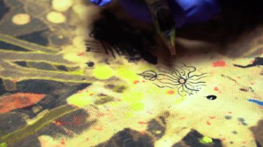 Elbiseleri akrilik boyalarla boyamak ve kumaşın üzerine mavi lastik eldivenli bir dövme makinesinin yardımıyla beyazlatıcı sürmek.