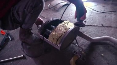 Eski bir arabanın egzoz sisteminin tamiri, öğütücüyle çalışmak, kaynak yapmak, gürültü emici yün yerleştirmek.