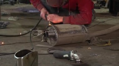 Eski bir arabanın egzoz sisteminin tamiri, öğütücüyle çalışmak, kaynak yapmak, gürültü emici yün yerleştirmek.