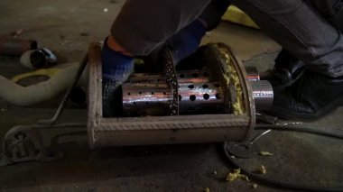 Eski bir arabanın egzoz sisteminin tamiri, öğütücüyle çalışmak, kaynak yapmak, gürültü emici yün yerleştirmek.