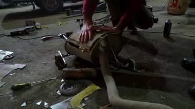Eski bir arabanın egzoz sisteminin tamiri, öğütücüyle çalışmak, kaynak yapmak, gürültü emici yün yerleştirmek.